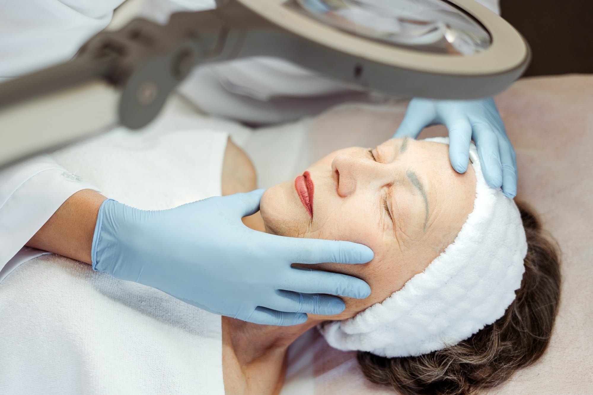 Elderly woman is lying, her face and skin being examined by cosmetologist, doing cosmetic procedures