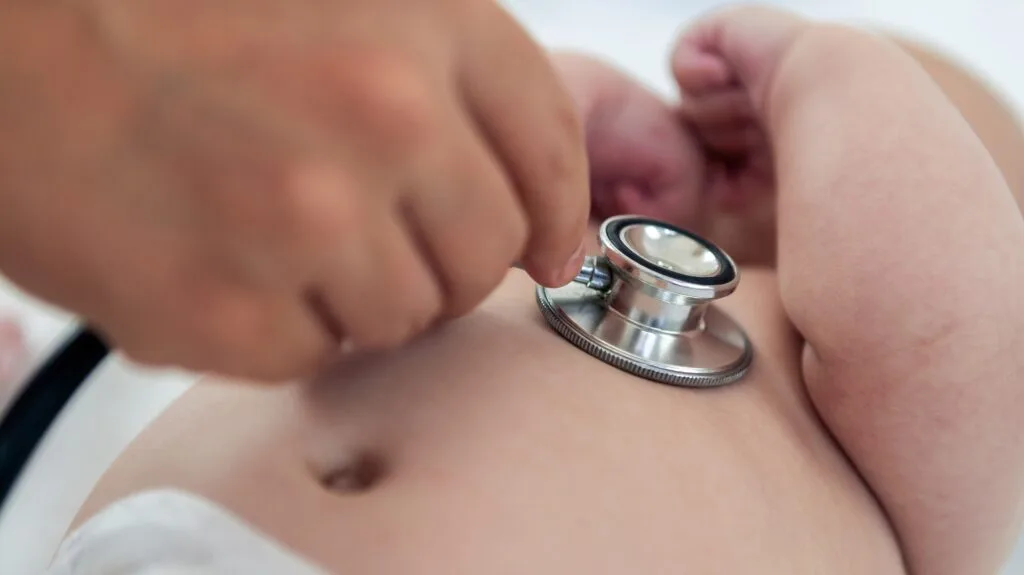 Female doctor examining baby boy toddler listening to lungs with stethoscope.